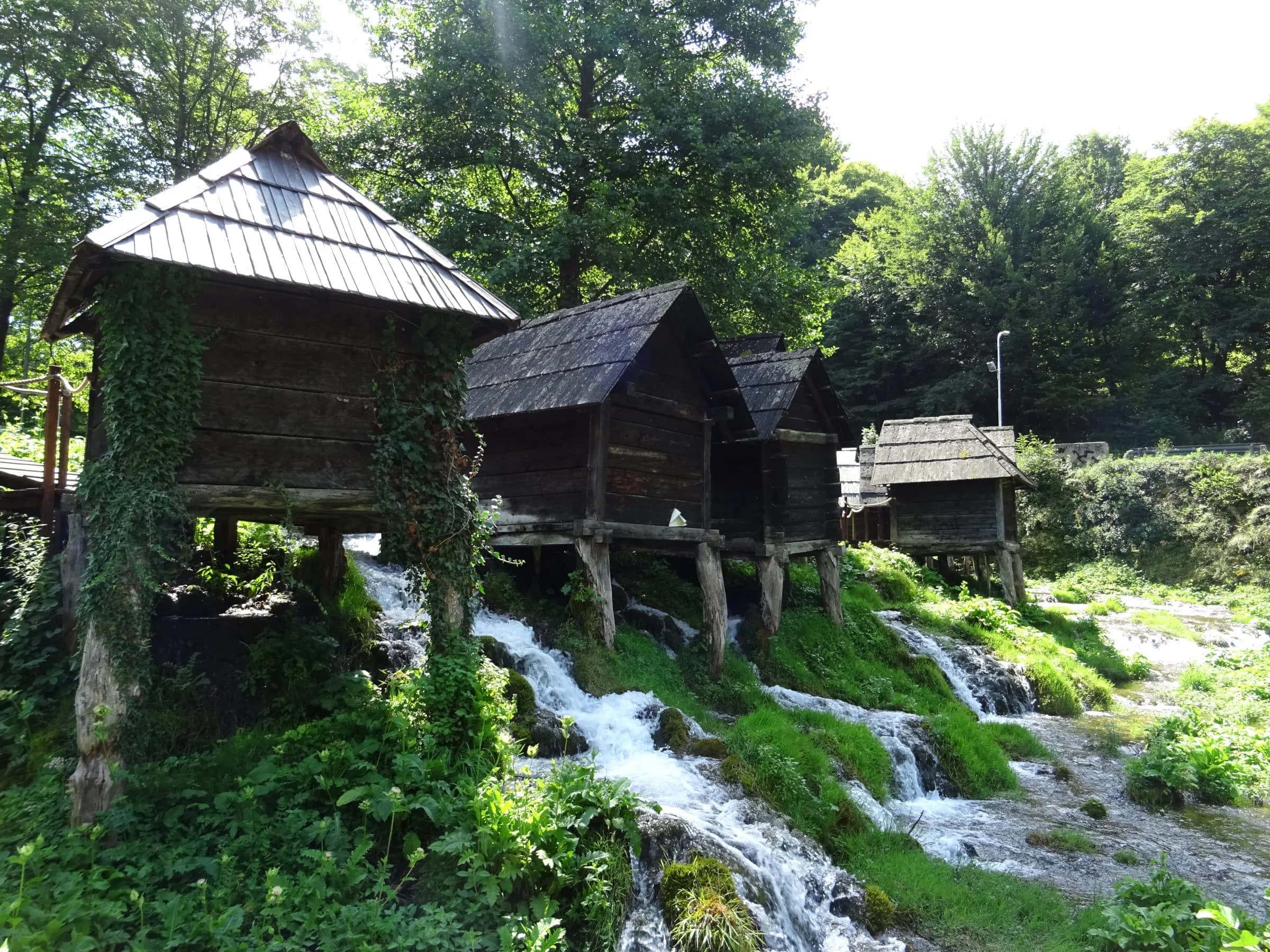 Hölzerne Wassermühlen (Mlinčići) auf Pfählen über kleinen Kaskaden der Pliva, umgeben von Bäumen